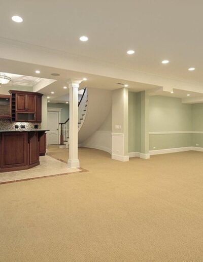 An empty, carpeted interior with a kitchenette and staircase.