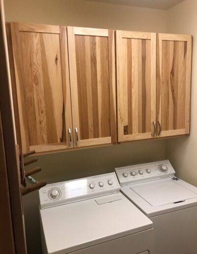 A laundry room with a top-loading washing machine, a front-loading dryer, and wooden cabinets above.