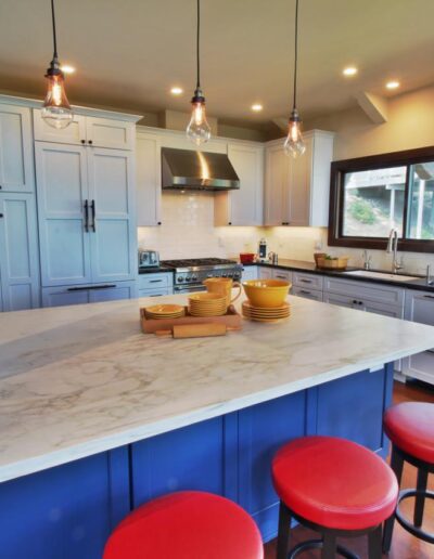 Modern kitchen interior with blue cabinets, marble countertops, and red bar stools.