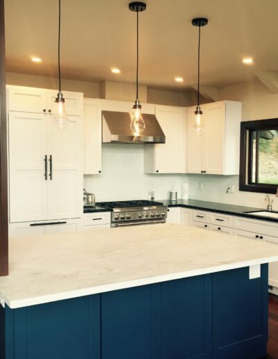 Modern kitchen with white cabinets, a blue island, stainless steel appliances, and pendant lighting.