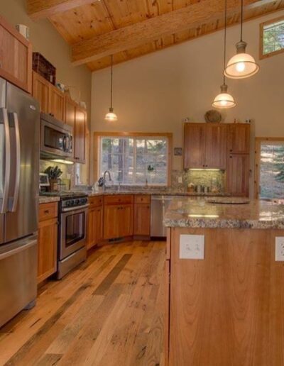 A well-lit, spacious kitchen with wooden cabinetry, stainless steel appliances, and hardwood flooring.