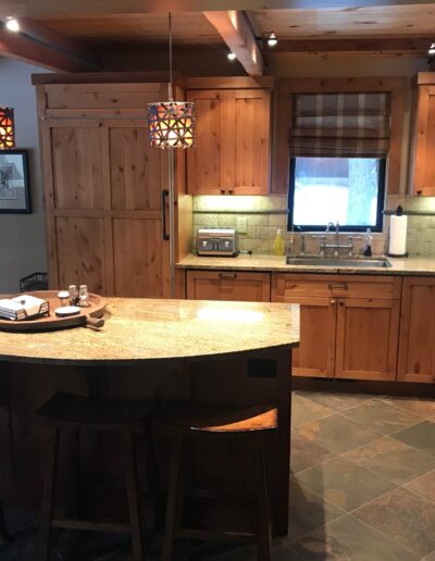 A well-lit kitchen with wooden cabinetry, granite countertops, and a central island with bar stools.