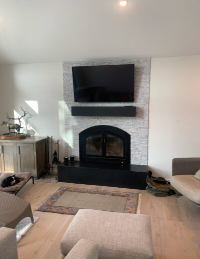 A modern living room with a mounted television above a stone fireplace, flanked by furniture and decor items.